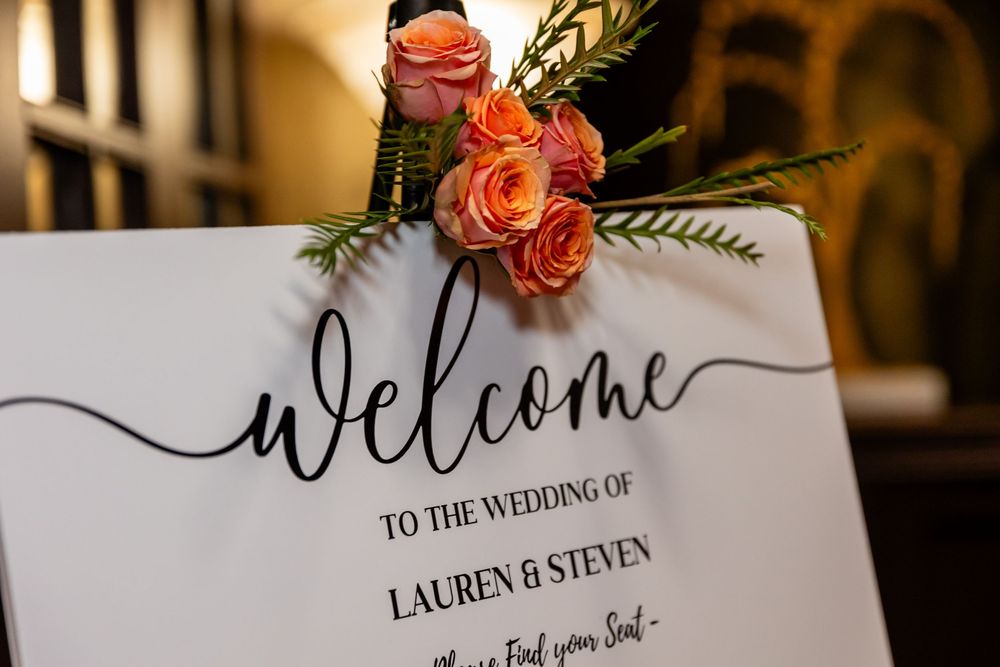 Elegant wedding welcome sign for Lauren & Steven decorated with orange roses and greenery.