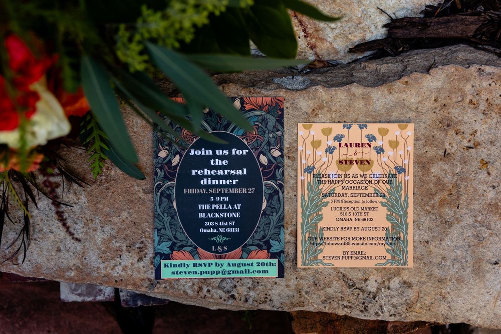 Two elegant wedding rehearsal dinner invitations displayed on a rustic stone surface with floral decorations.