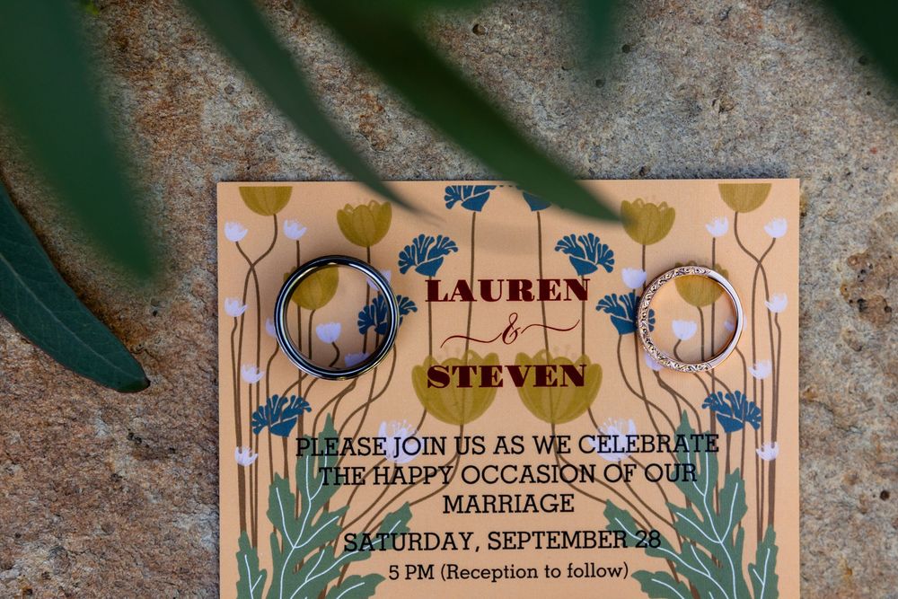 Gold floral wedding invitation for Lauren and Steven, Saturday September 28, with rings resting on top.