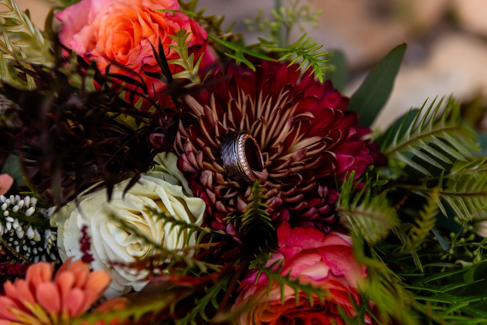 Close-up of a diamond ring nestled in a vibrant bridal bouquet with dark burgundy dahlias and pink roses.
