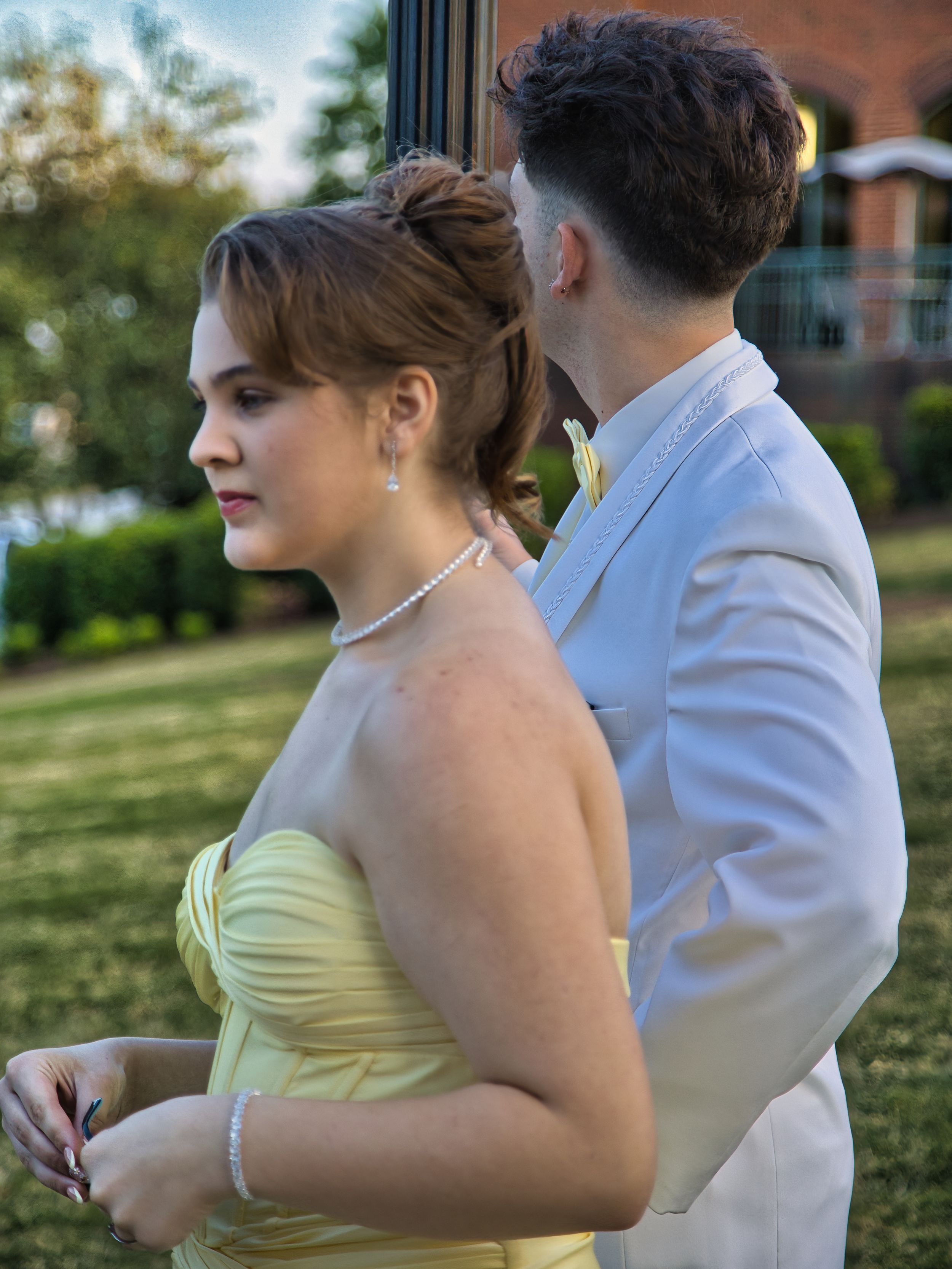 Prom couple outdoors at sunset, girl in yellow strapless gown with boy in white tuxedo.