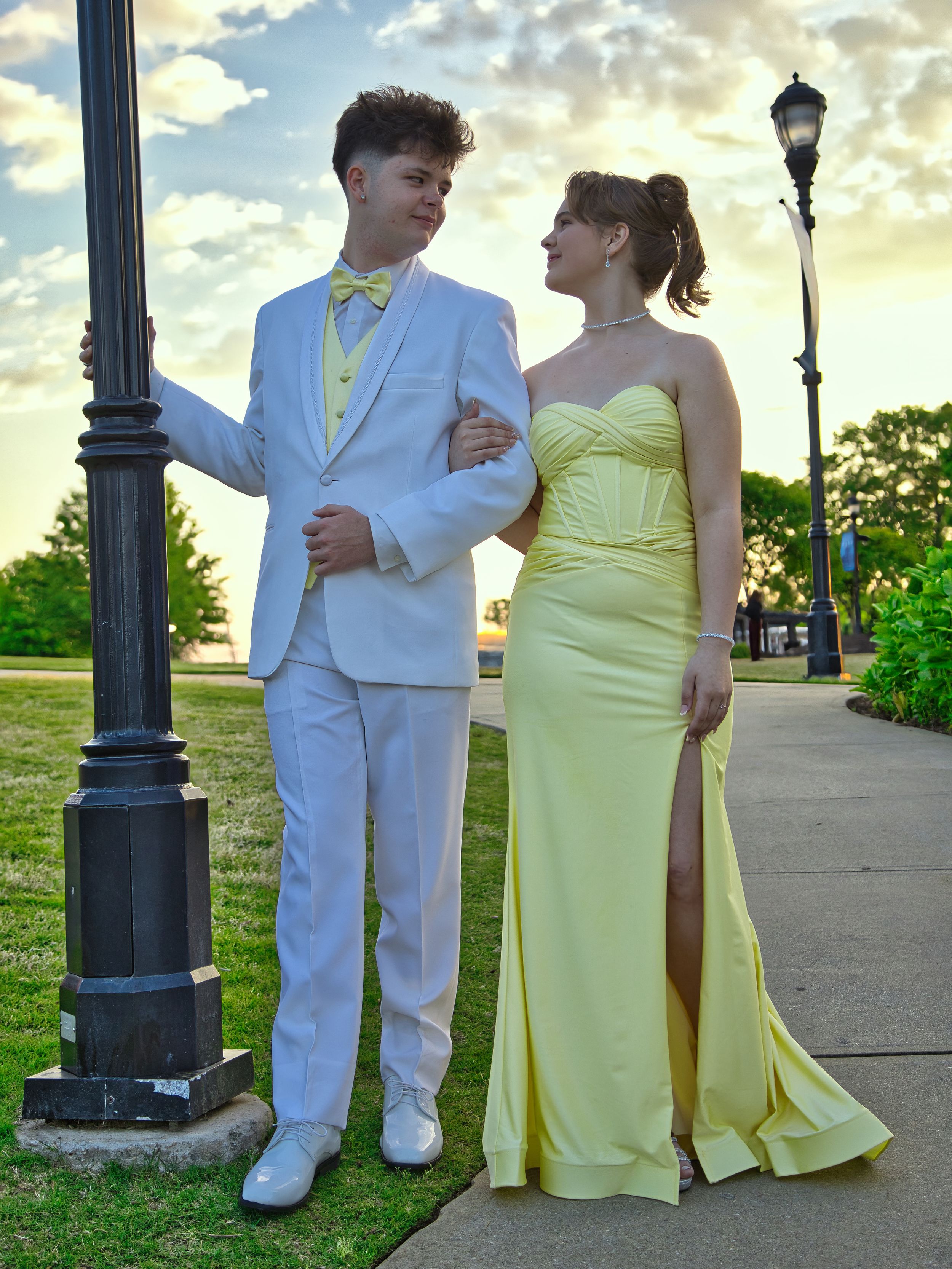 Prom couple posing by lamppost at sunset, boy in white tux and girl in yellow formal gown.