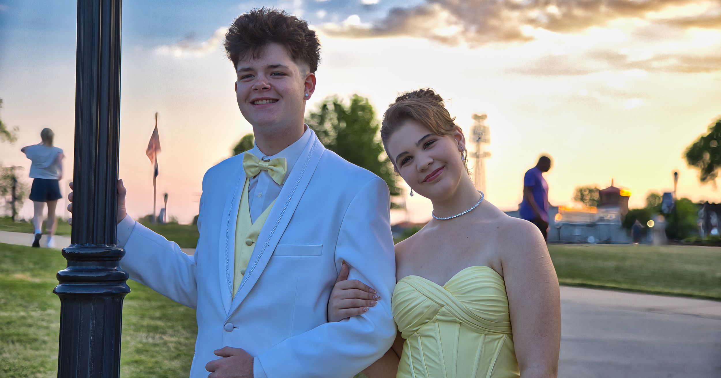 Happy prom couple smiling together outdoors at sunset in coordinating yellow and white outfits.