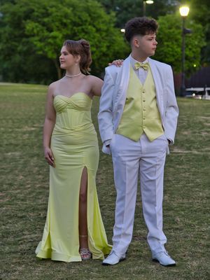 Prom couple posing outdoors in coordinating yellow strapless gown and white suit with yellow vest.