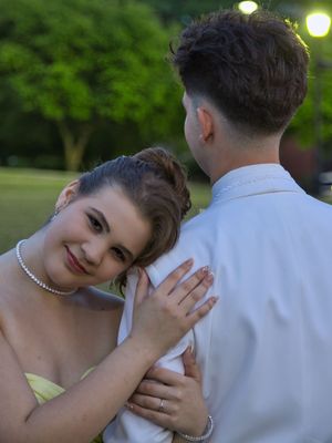 Young couple in matching yellow and white prom attire share a tender moment outdoors at dusk.