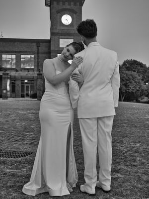 Black and white photo of prom couple embracing near historic clock tower building at dusk.
