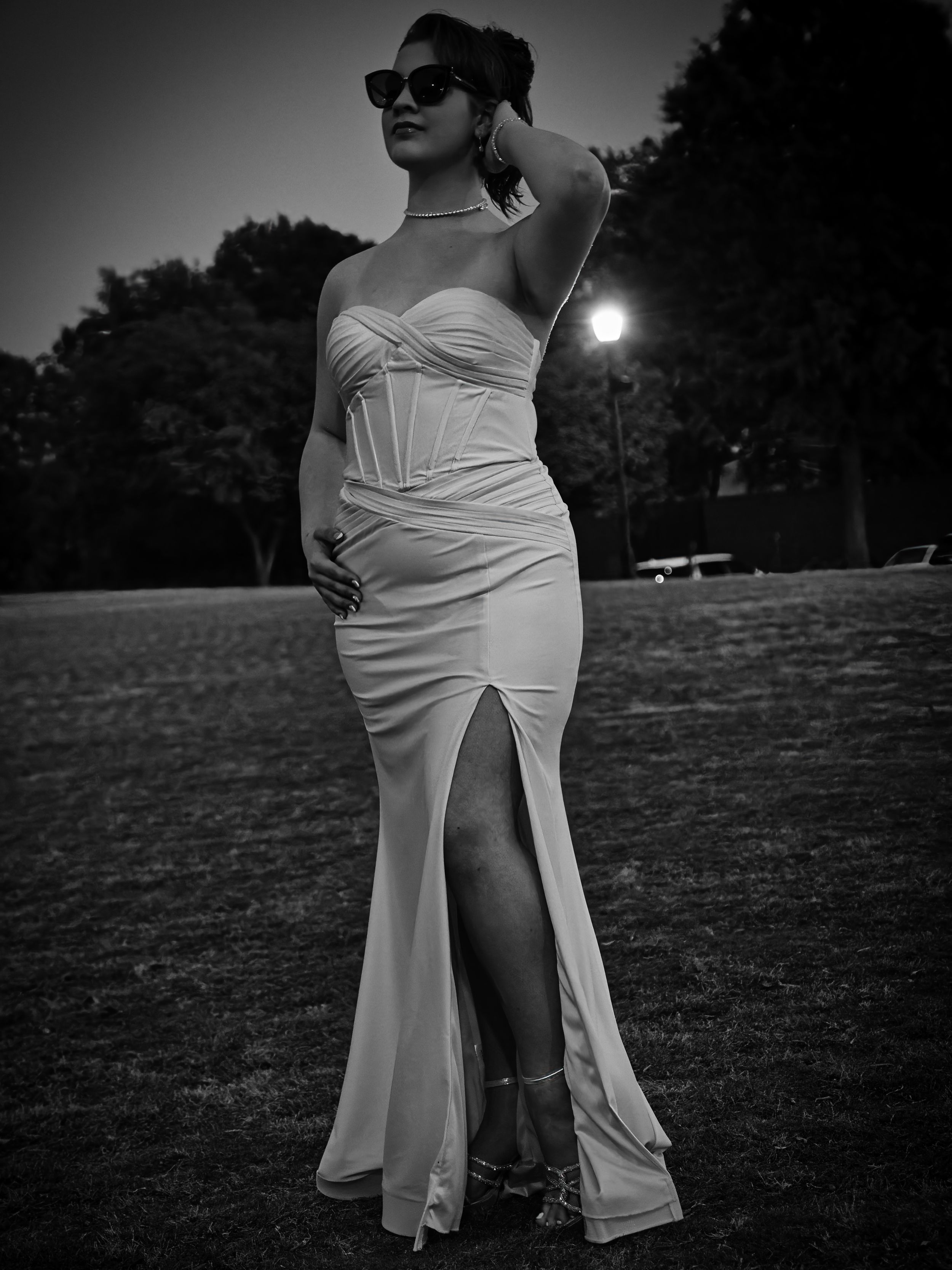 Elegant black and white photo of woman in strapless gown with slit posing outdoors at night.