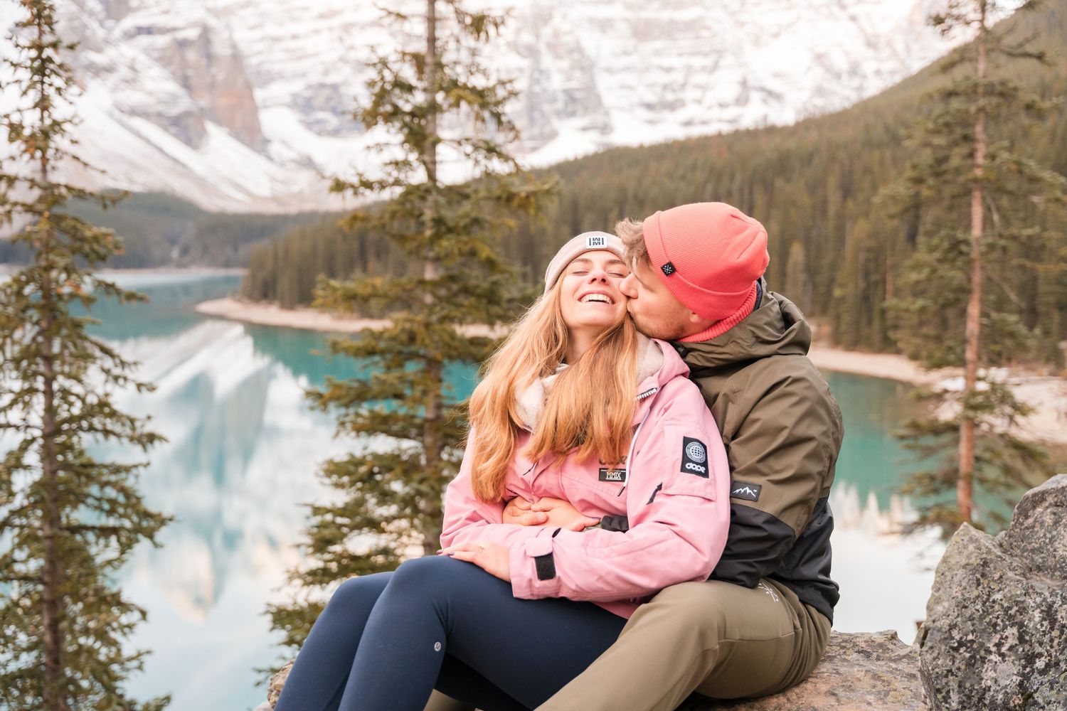 Couple sharing a romantic kiss at Moraine Lake, Banff, with turquoise water and snow-capped mountains in the background.