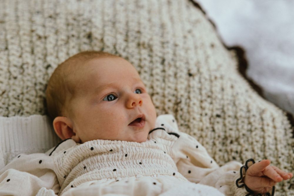 Adorable newborn baby lying on a cozy knit blanket, looking up with curious blue eyes in soft natural light.