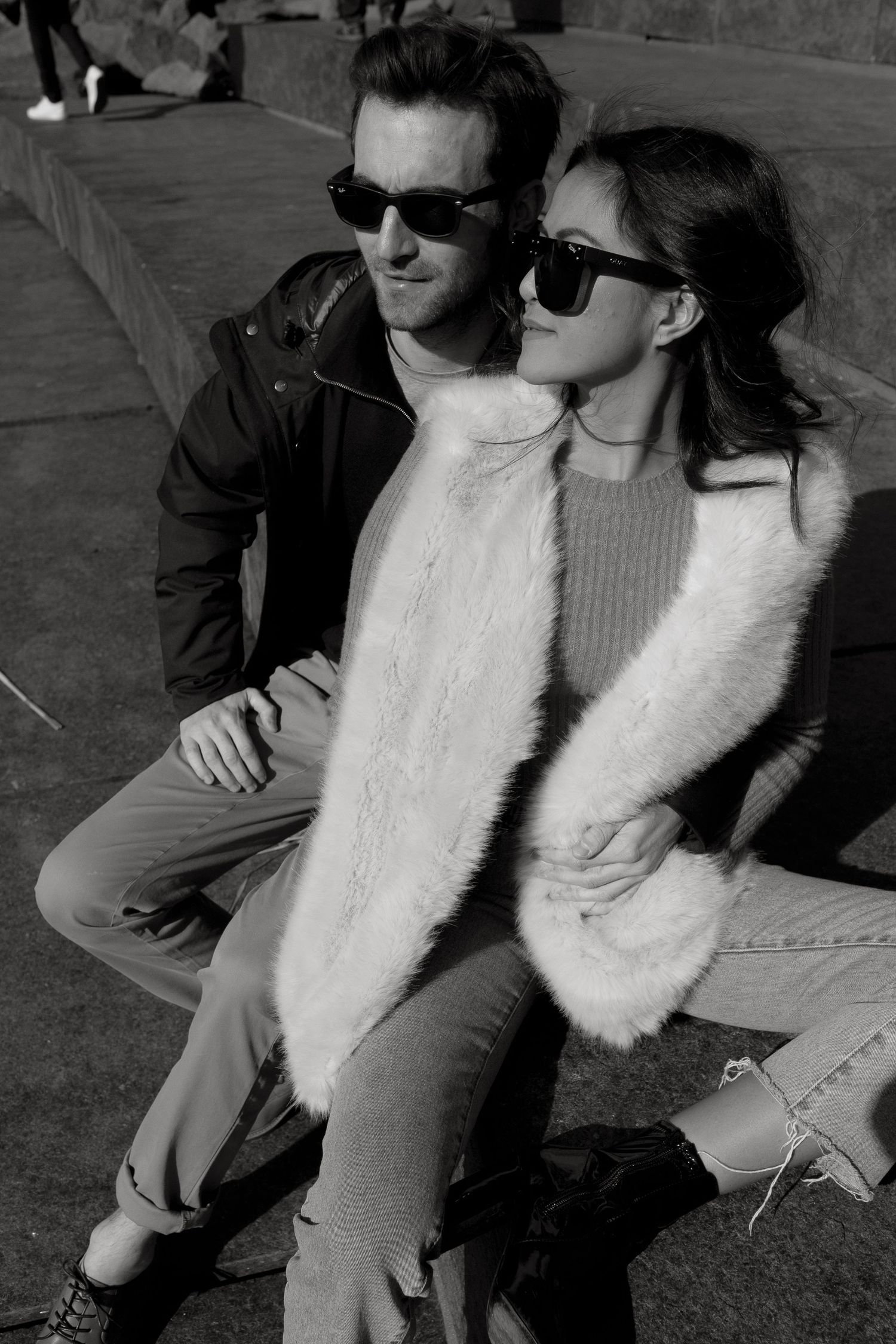 Black and white photo of a smiling couple, man giving woman a piggyback ride on a NYC street with Manhattan Bridge backdrop.