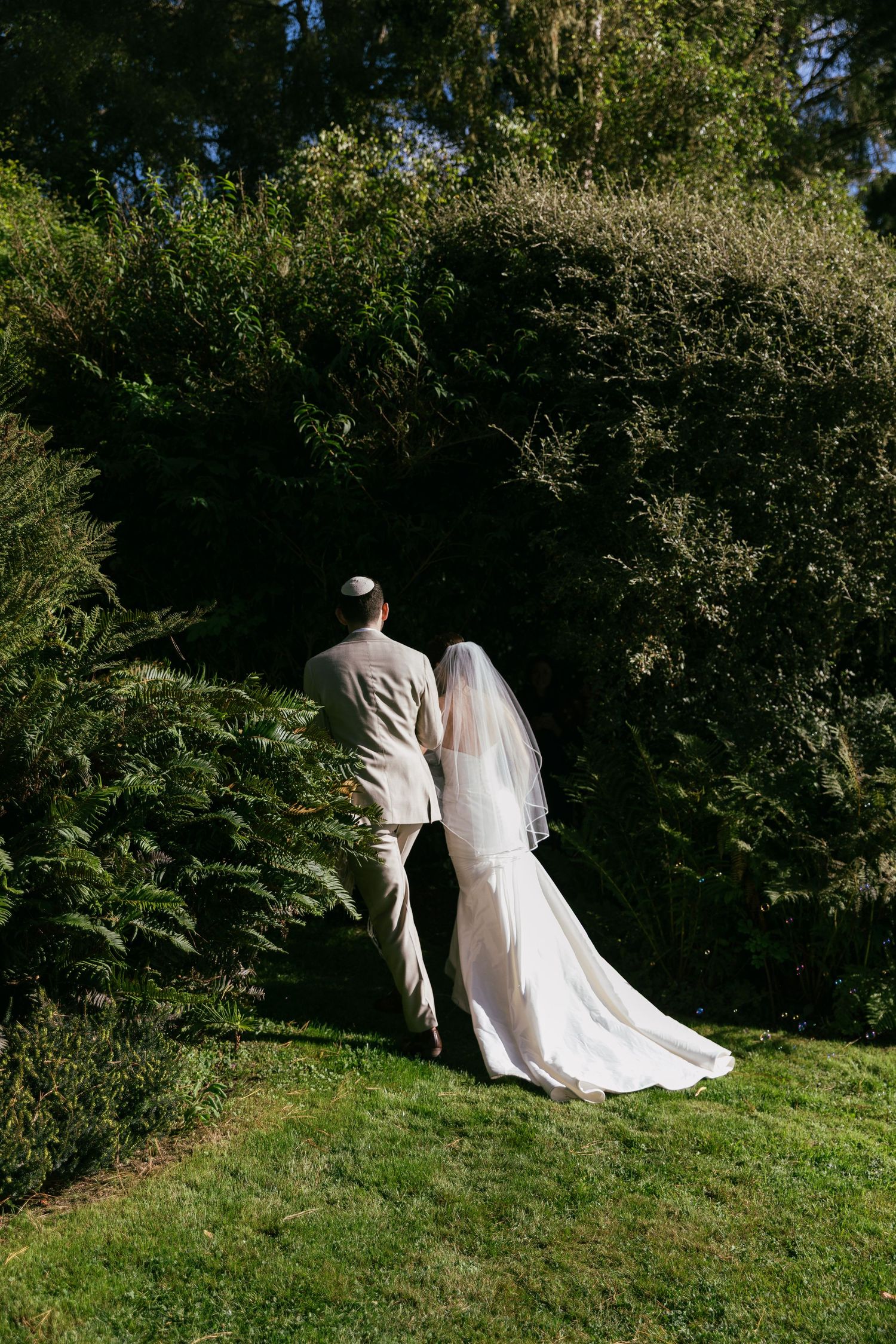 Bride and groom walking hand in hand through lush green garden.
