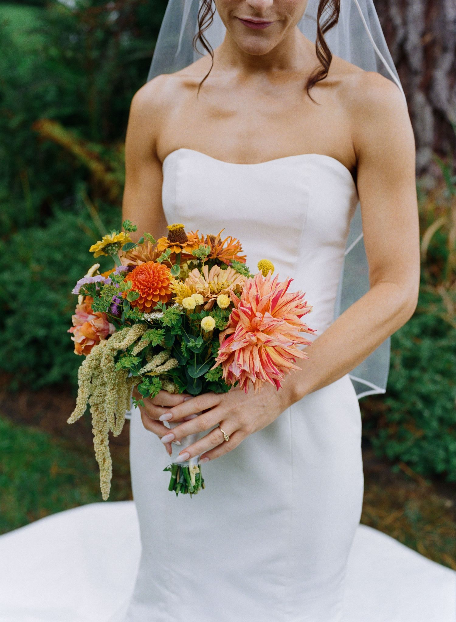 Bride in strapless white gown holding a vibrant orange and pink dahlia wedding bouquet.