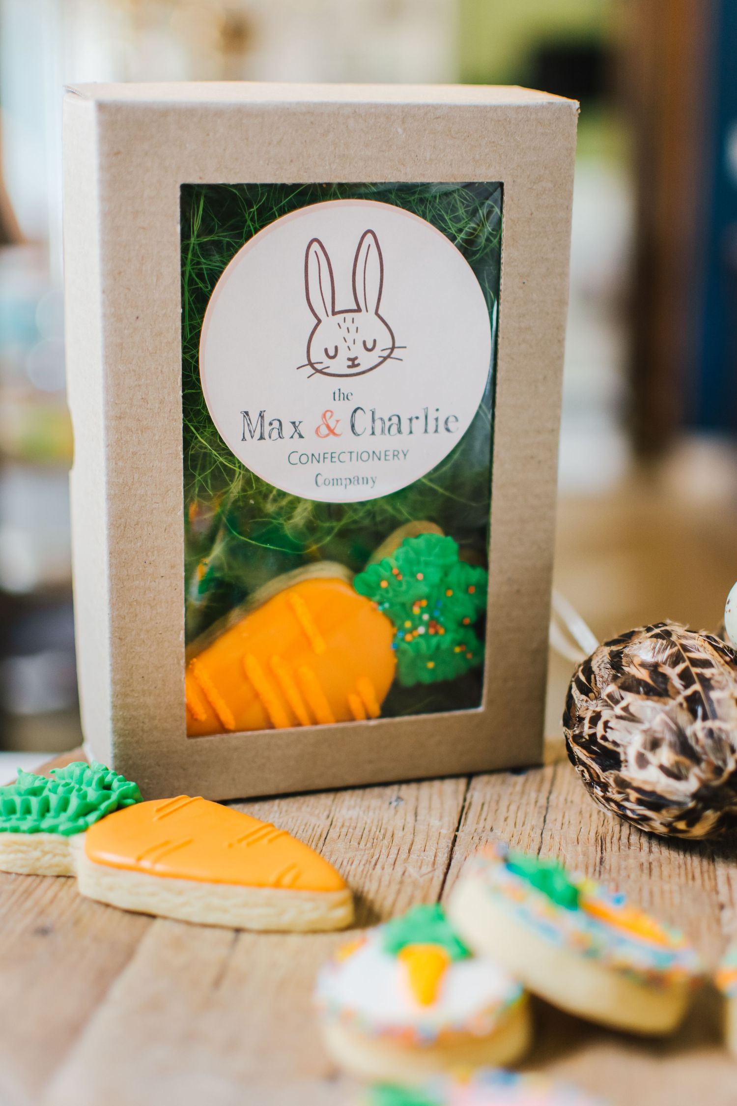Max & Charlie Confectionery Co. Easter cookie gift box with decorated carrot and bunny sugar cookies on wooden table.