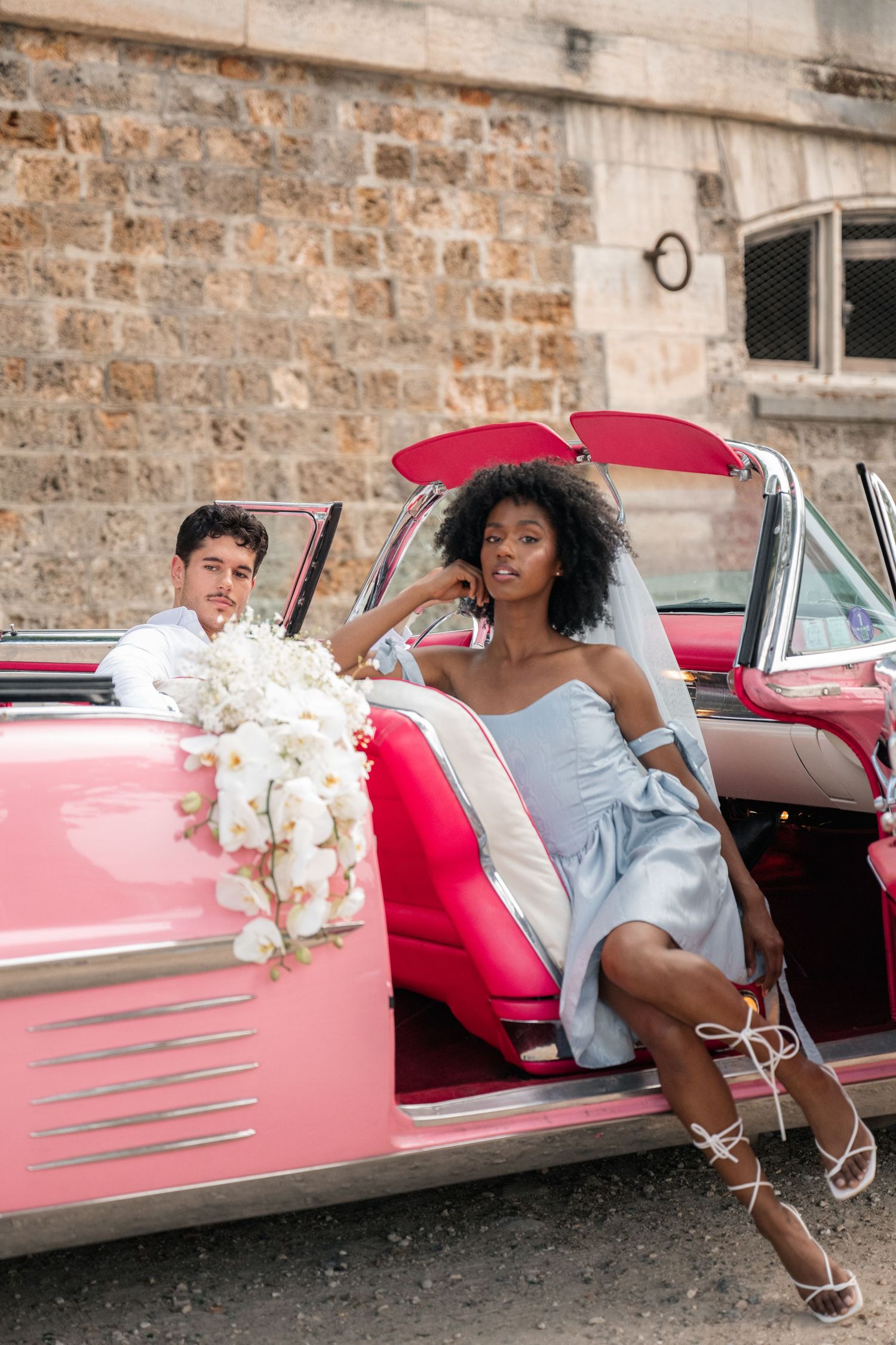 Three stylish lifestyle photos feature a model posing elegantly with a retro pink classic car against a stone wall backdrop.