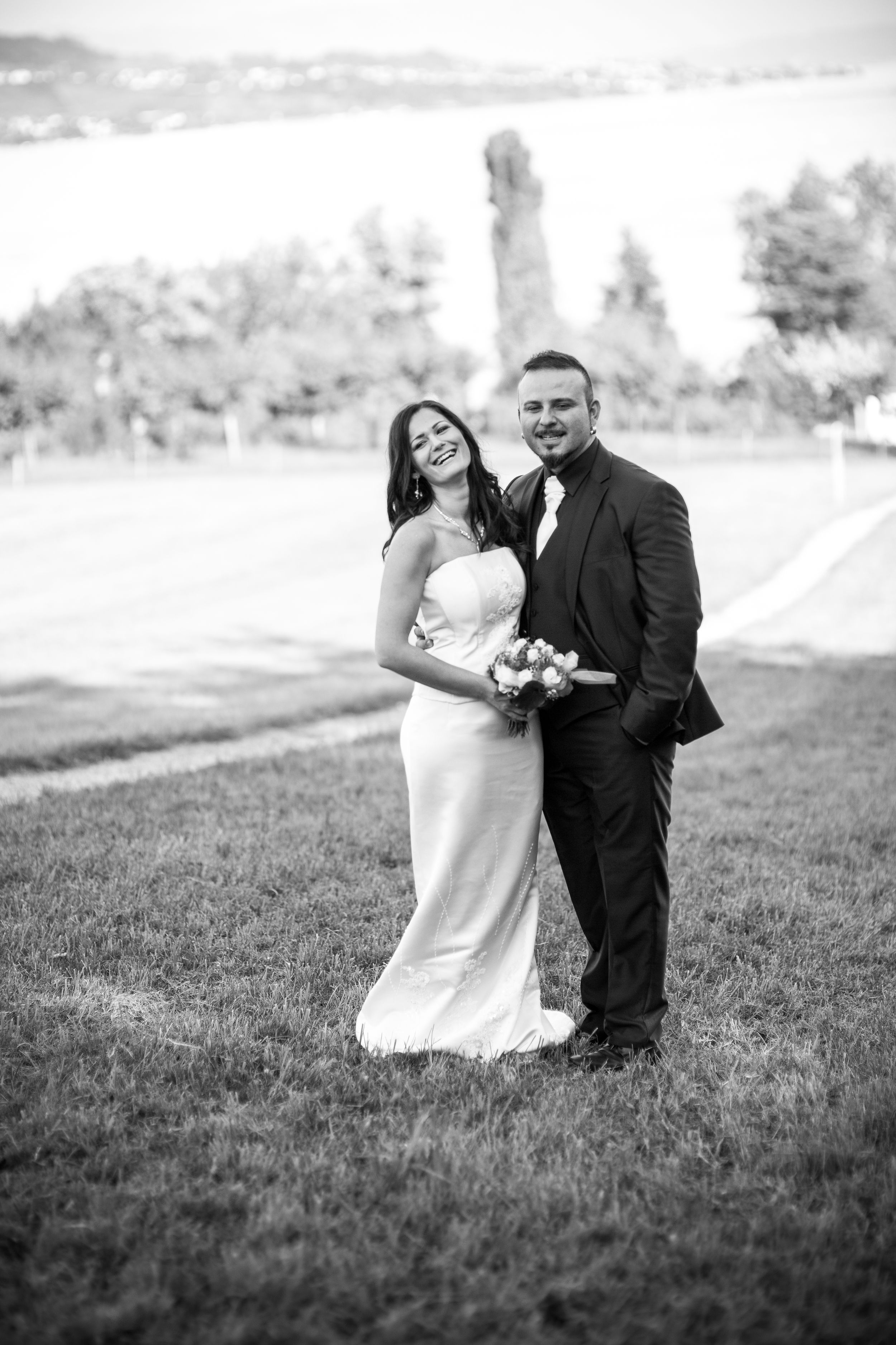 Happy newlywed couple posing together on green grass in black and white wedding photography outdoors.