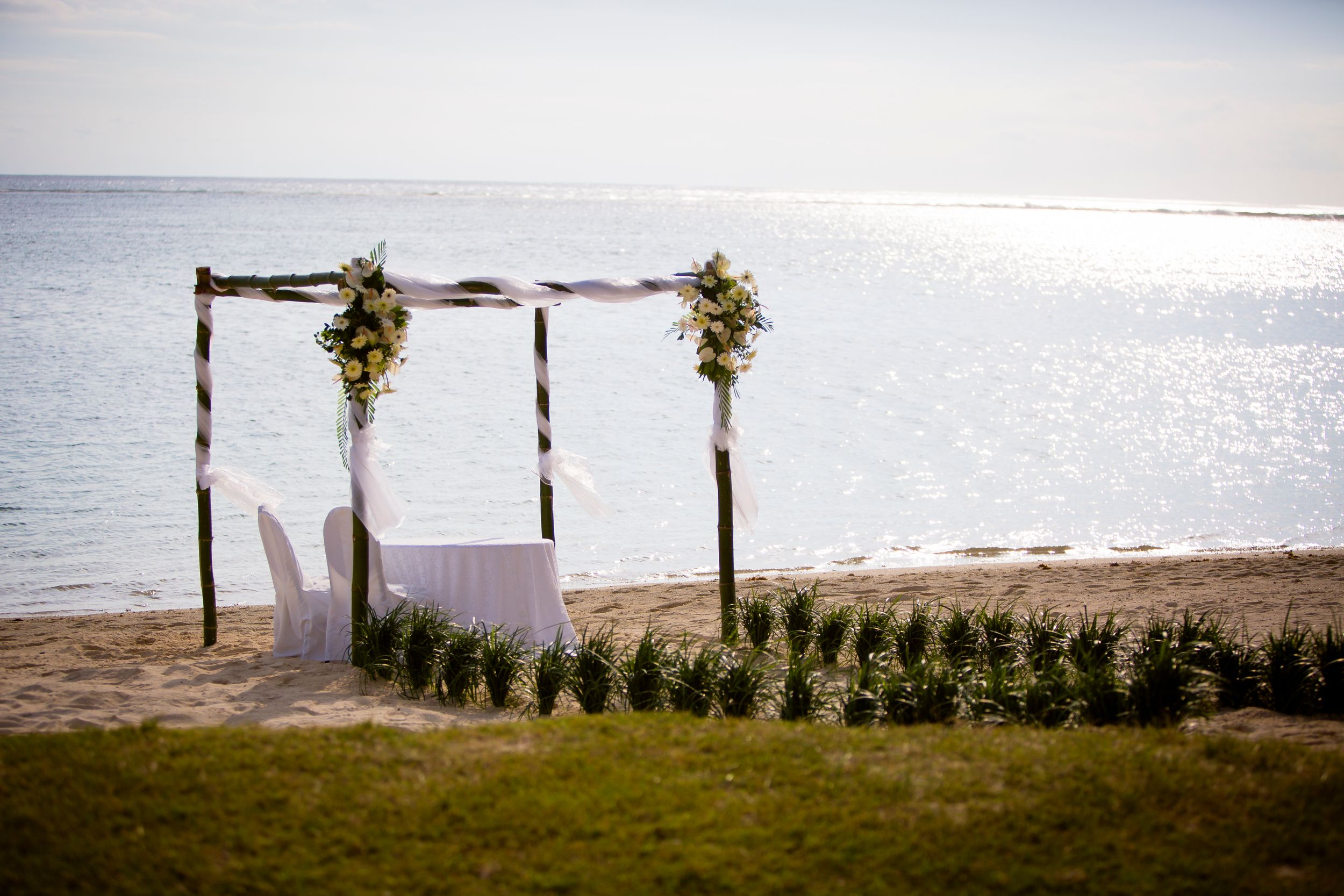 Elegant beach wedding ceremony setup with floral arch on sandy shore overlooking calm ocean waters.