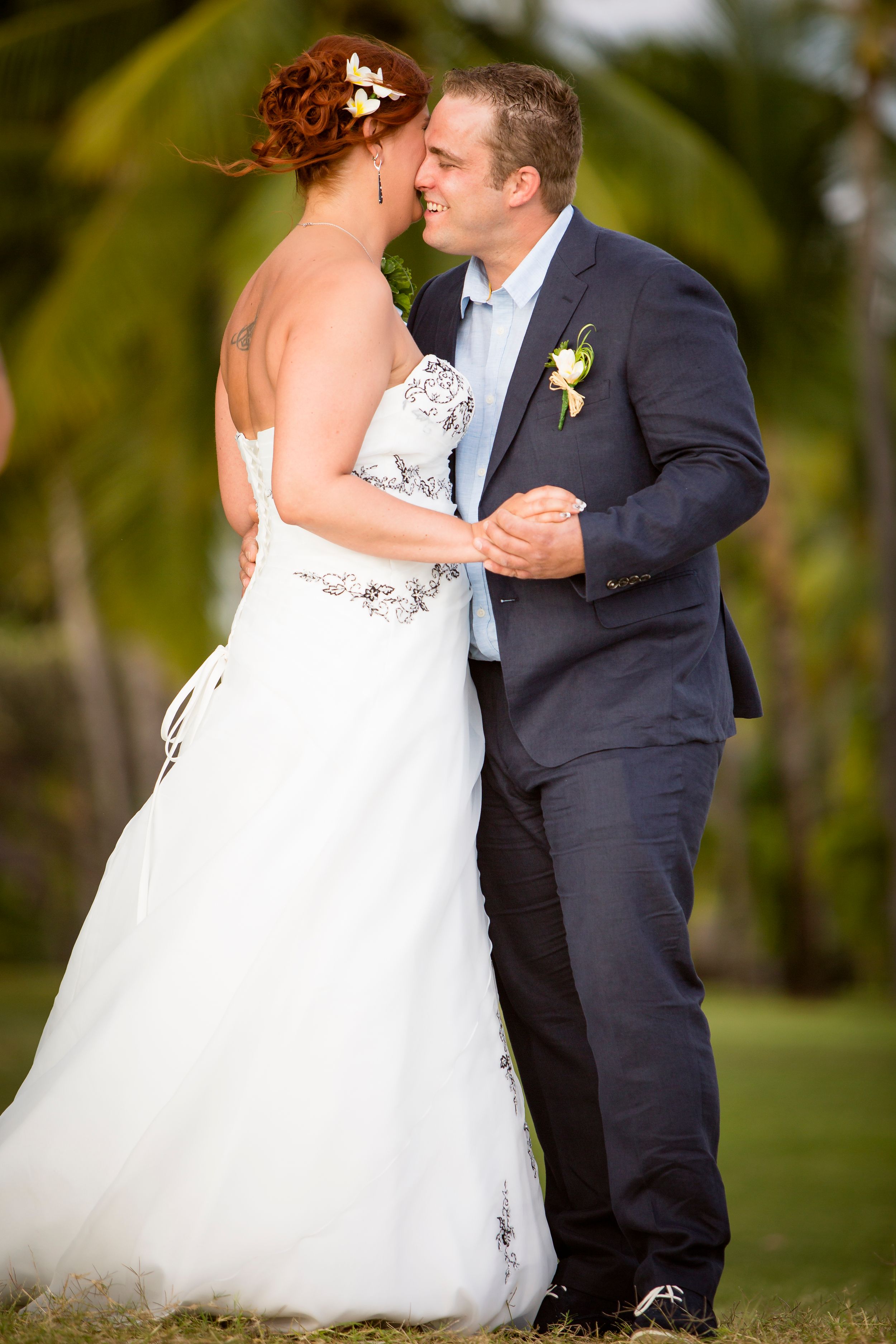 Bride and groom sharing a romantic moment about to kiss outdoors with tropical palm trees in background.