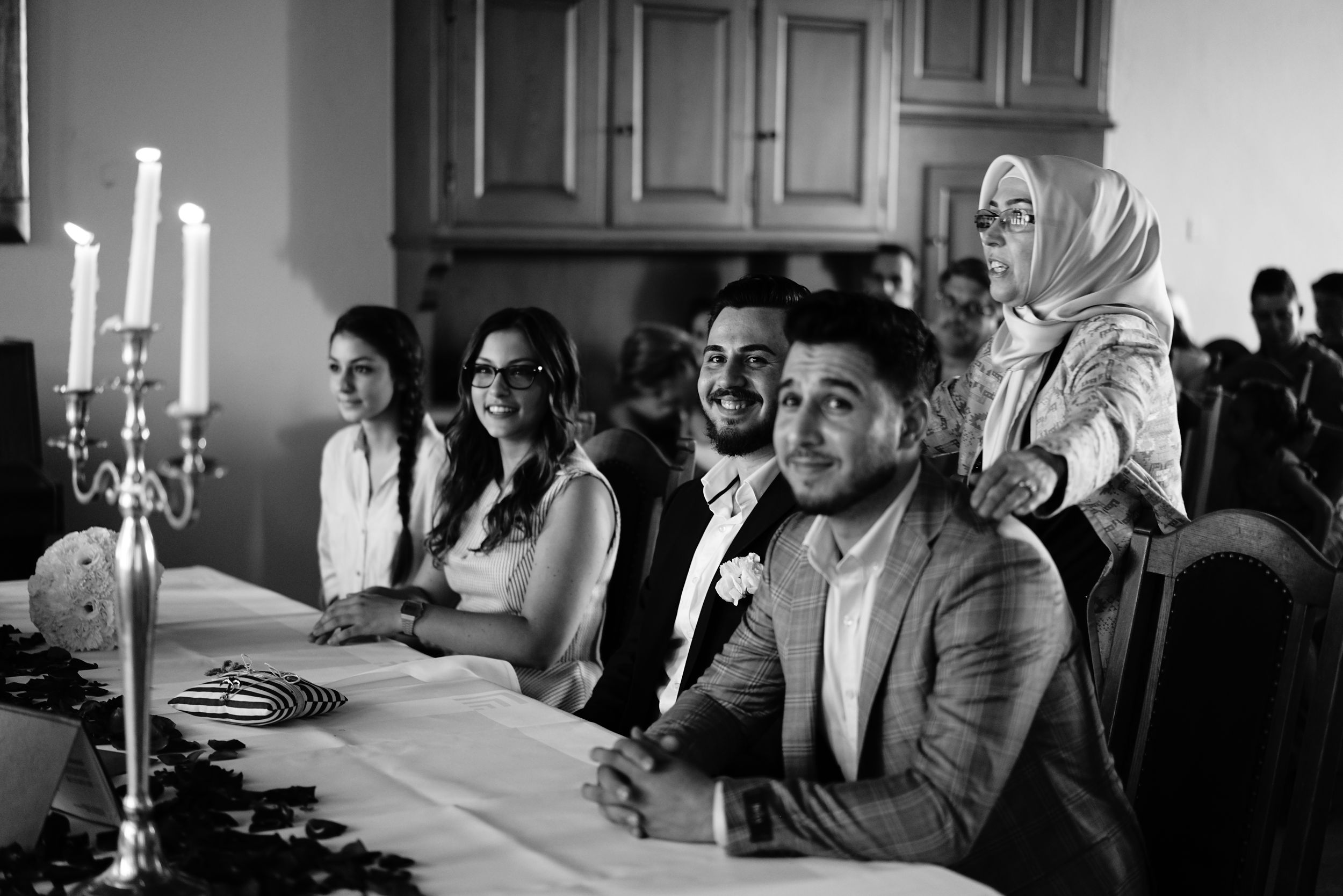 Wedding guests smiling and laughing at a reception table with candelabras in a black and white photo.