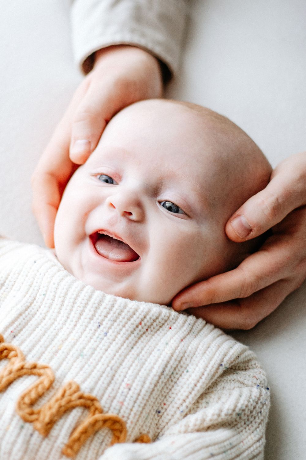 Parents lovingly gazing at their newborn baby lying between them on a white surface in a bright studio.