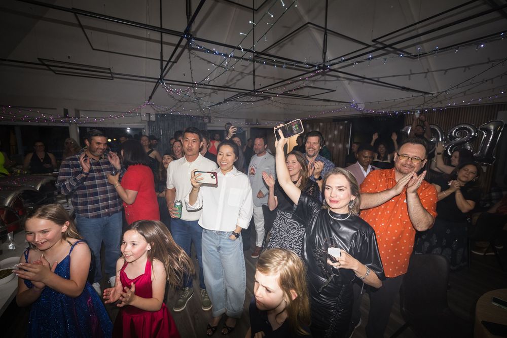 Crowd of people celebrating at an indoor party event under a tent with festive lighting and decorations.