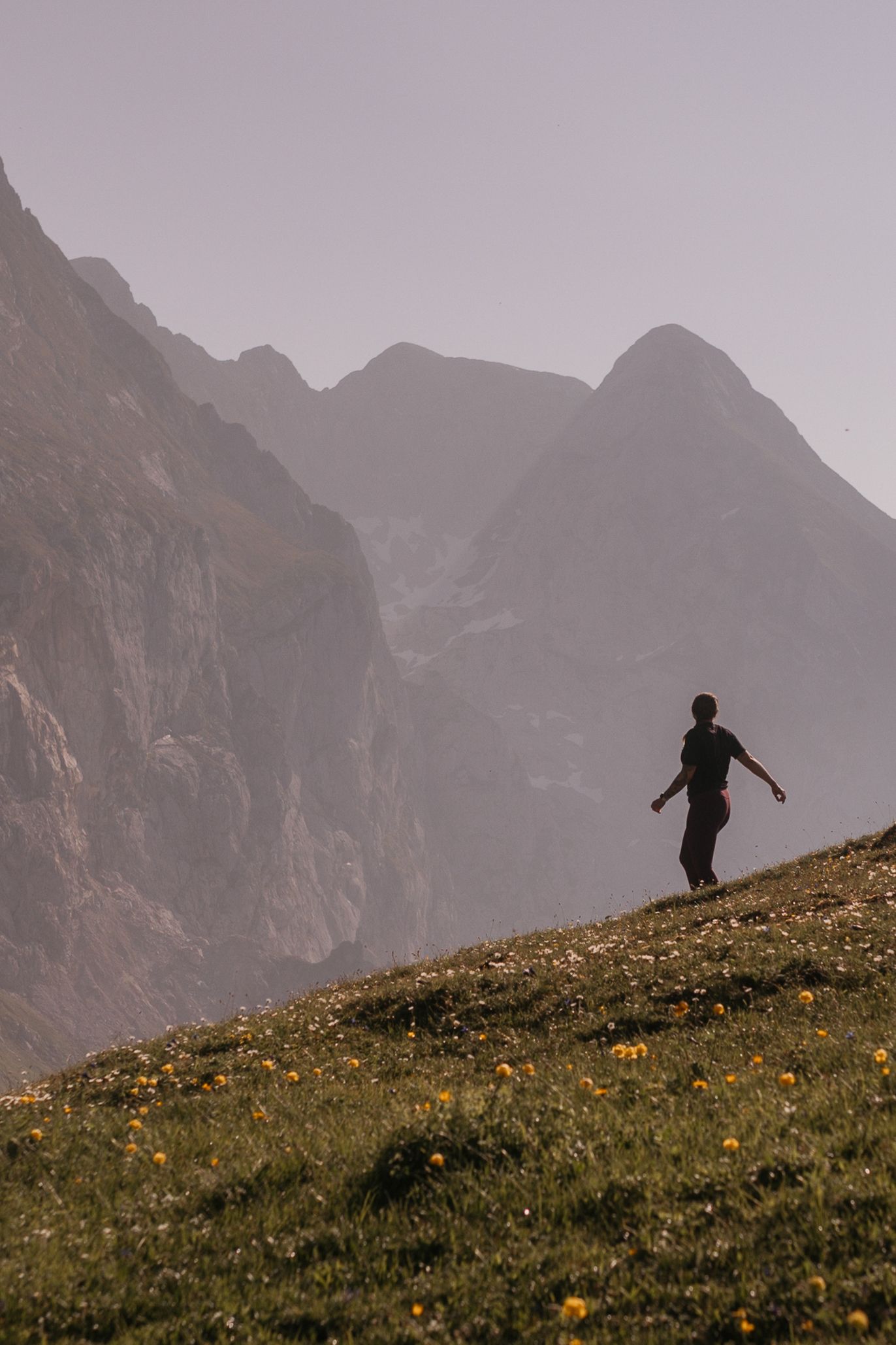 Hiker with green backpack ascending rocky mountain trail with alpine lake and peaks in background on clear day.
