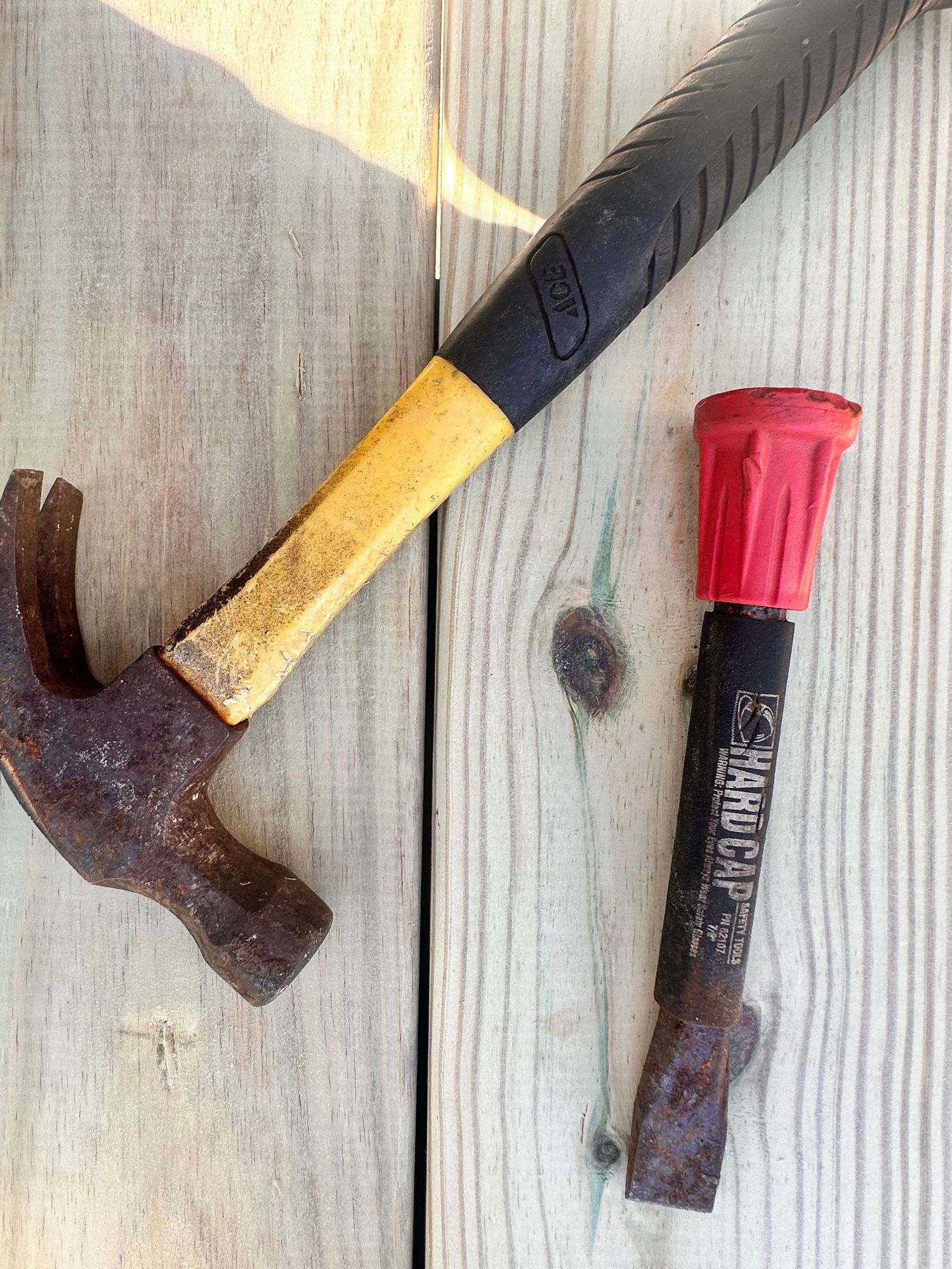 Two rusty tools on wood surface: a claw hammer with yellow handle and a chisel with red cap.
