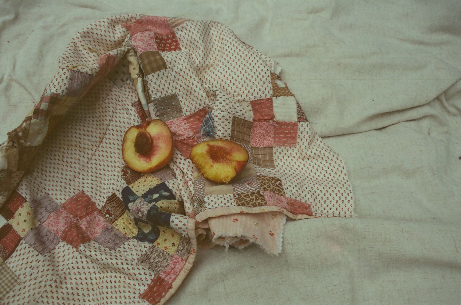 Vintage patchwork quilt in pink and cream tones displayed with fresh peach fruit on white fabric background.