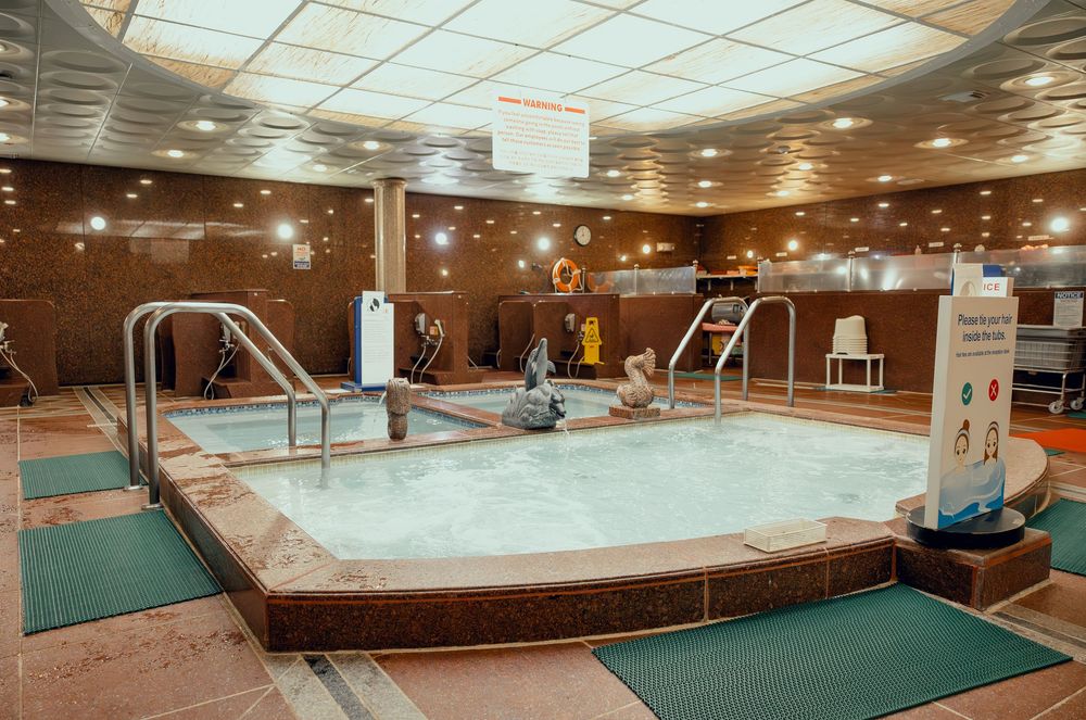 Indoor hotel spa jacuzzi pool with bubbling water, tiled surroundings, and safety equipment in a warm lit facility.