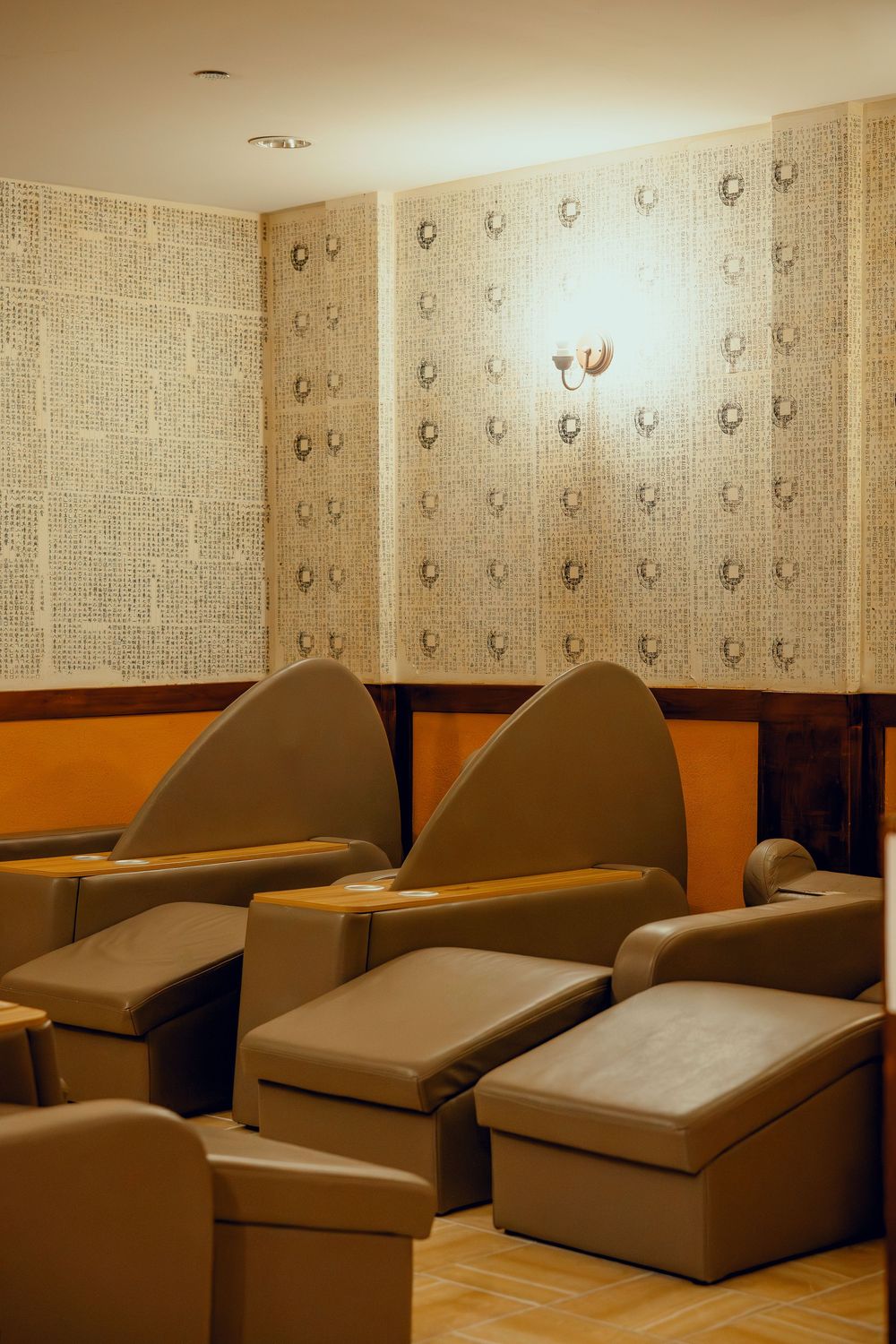 Luxurious spa pedicure lounge with brown leather recliner chairs and ottomans against patterned wallpaper.