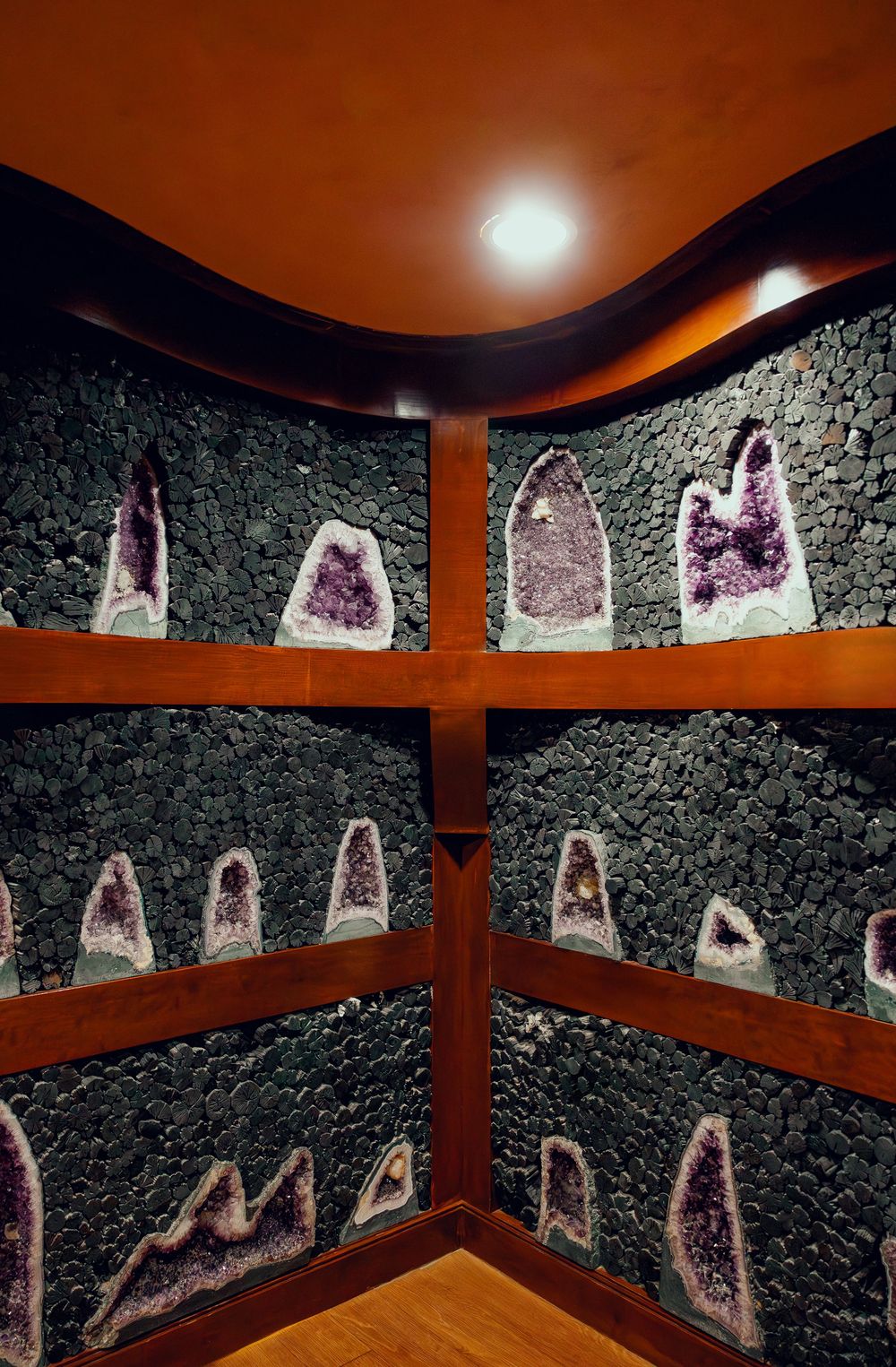 Corner display of amethyst crystal geodes mounted on dark pebble stone walls with wooden framing.