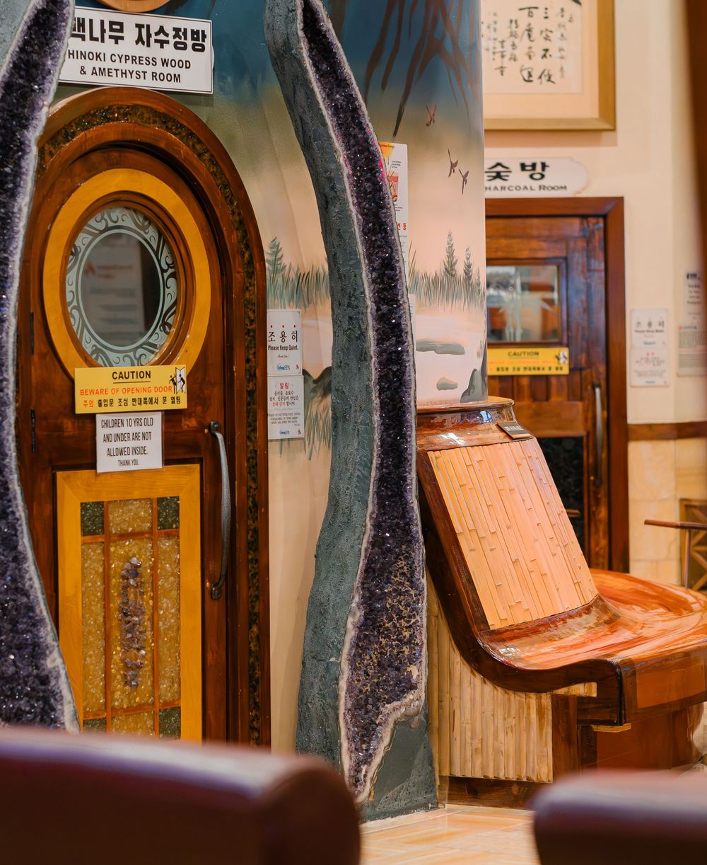 Korean spa interior featuring an amethyst geode doorway, hinoki cypress wood room entrance, and wooden relaxation chair.