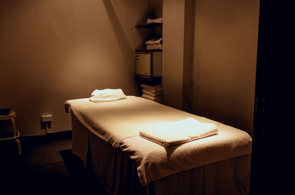 Dimly lit massage treatment room with a white-sheeted table, folded towels, and warm ambient lighting.