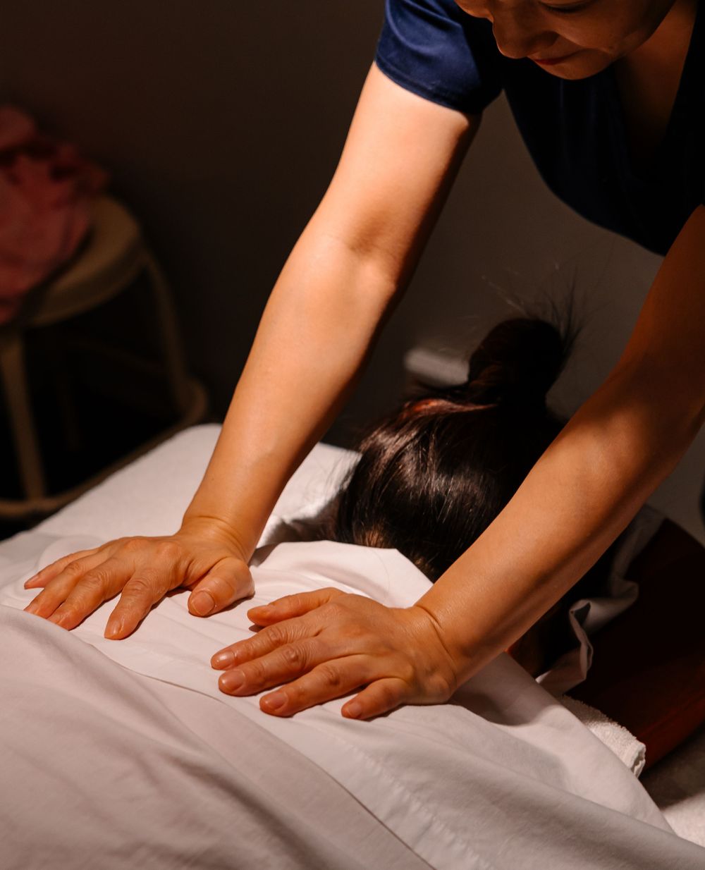 Massage therapist performing a relaxing back massage on a client lying on a white treatment table.