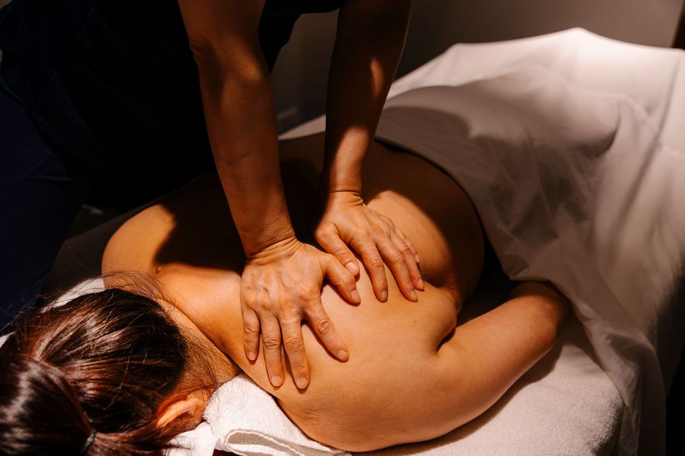 A massage therapist performing a deep tissue back massage on a client lying on a white spa table.