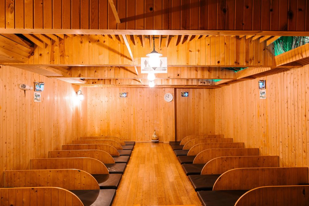 Rustic wooden sauna room with rows of benches, pine walls, and a hanging chandelier light fixture.