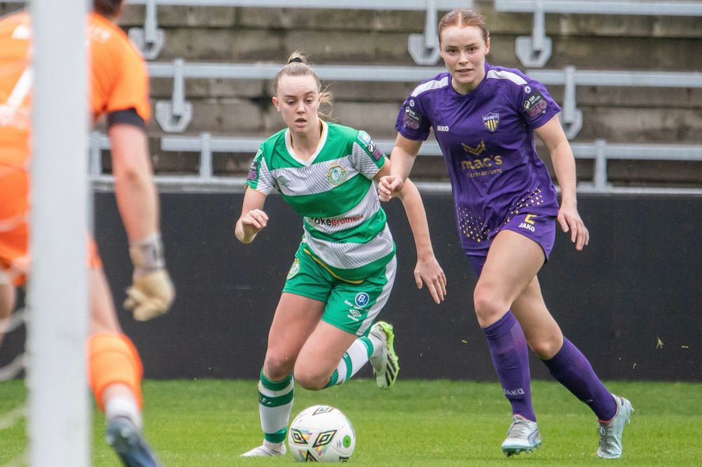 Two female soccer players in green and purple kits compete for the ball during a women's football match.