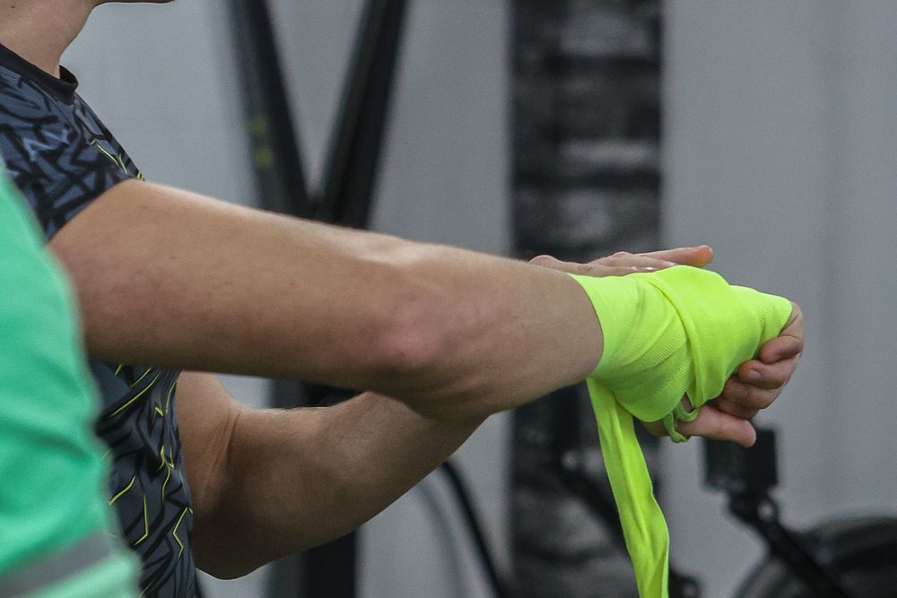 Athlete wrapping hands with neon green boxing hand wraps in gym.