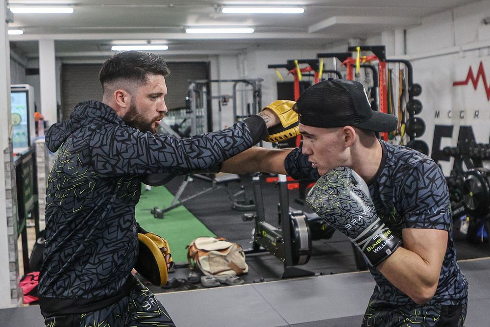 Two fighters sparring with punch mitts during boxing training session in gym.
