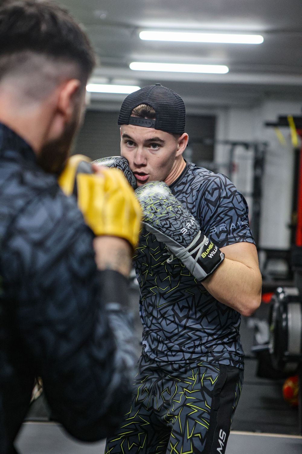 Young boxer throwing punch at focus mitts during intense gym training session.