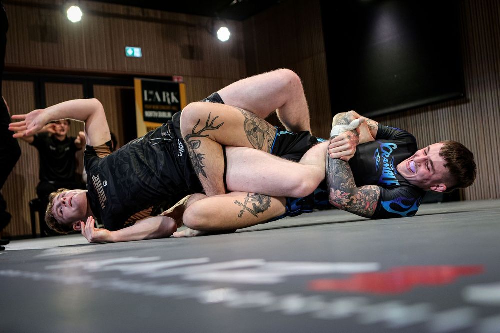 Two grapplers competing in submission wrestling match at indoor grappling event.