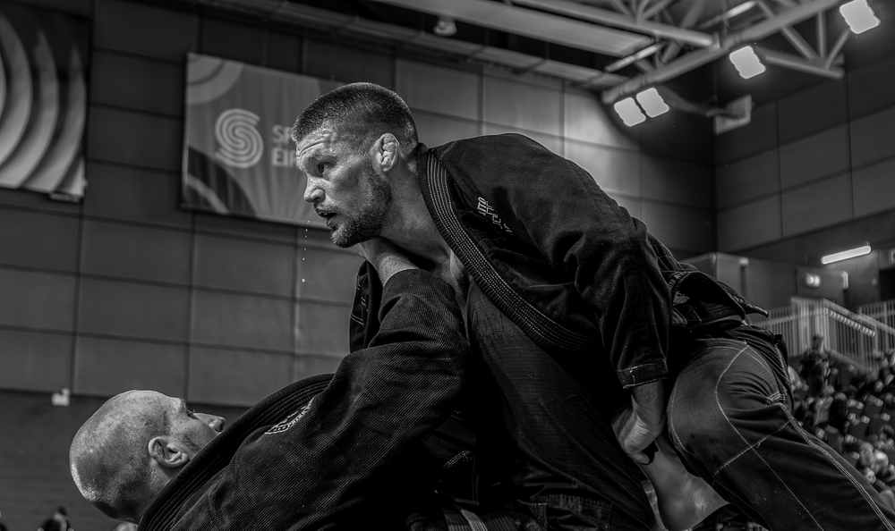 Two BJJ competitors grappling in black gis during a jiu-jitsu tournament in black and white.