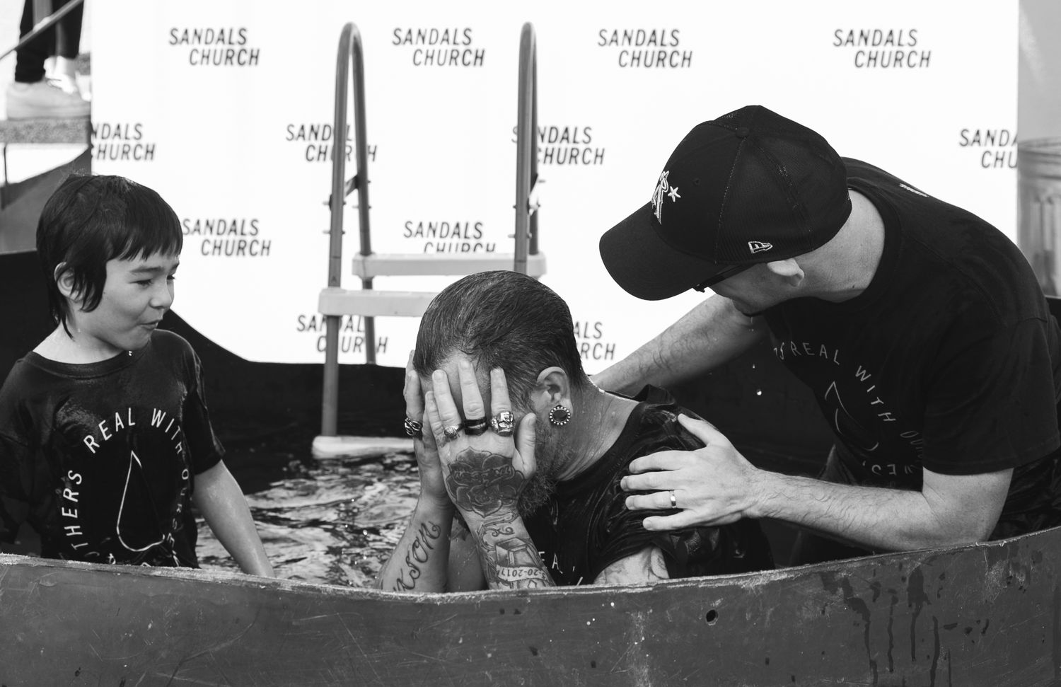 A baptism ceremony at Sandals Church with a person being immersed in water assisted by a pastor and child nearby.