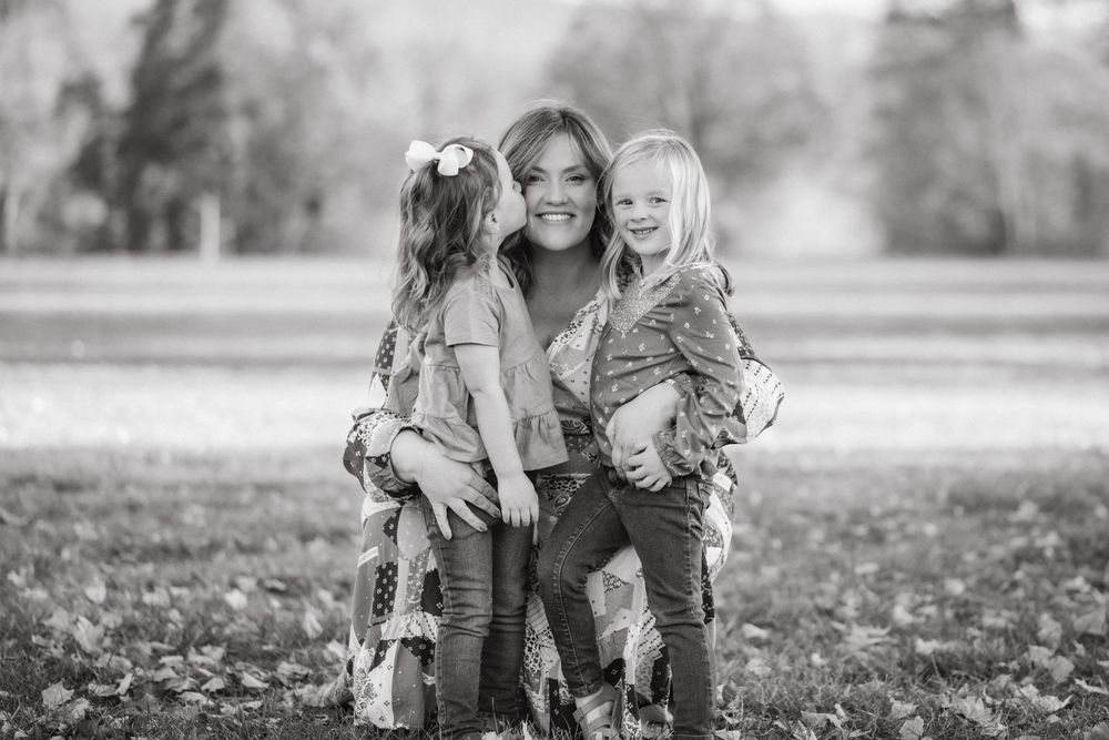 Black and white photo of a smiling woman hugging two young girls outdoors in a park setting in Johnson City, TN.