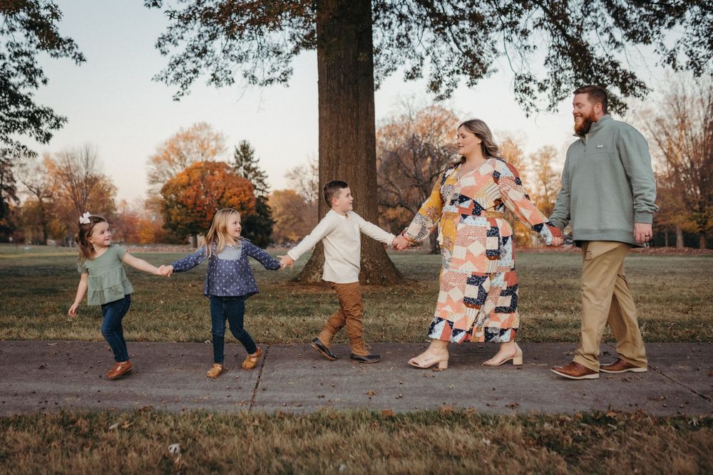 Family of five holding hands walking outdoors in a park during autumn, with colorful trees in the background in Johnson City, TN.