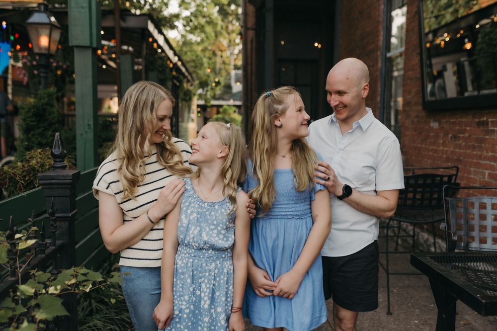 A happy family of four smiling and laughing together outdoors at a charming restaurant patio setting in Louisville, KY.