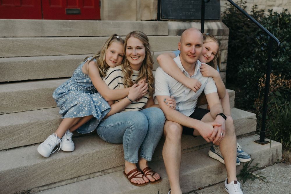 A happy family of four smiling together on stone steps outside a brick building in Louisville, KY.
