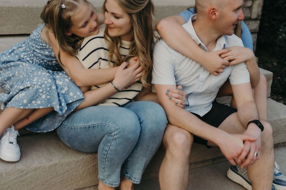 Family of three sitting on steps, parents and young girl sharing a warm embrace outdoors in Louisville, KY.
