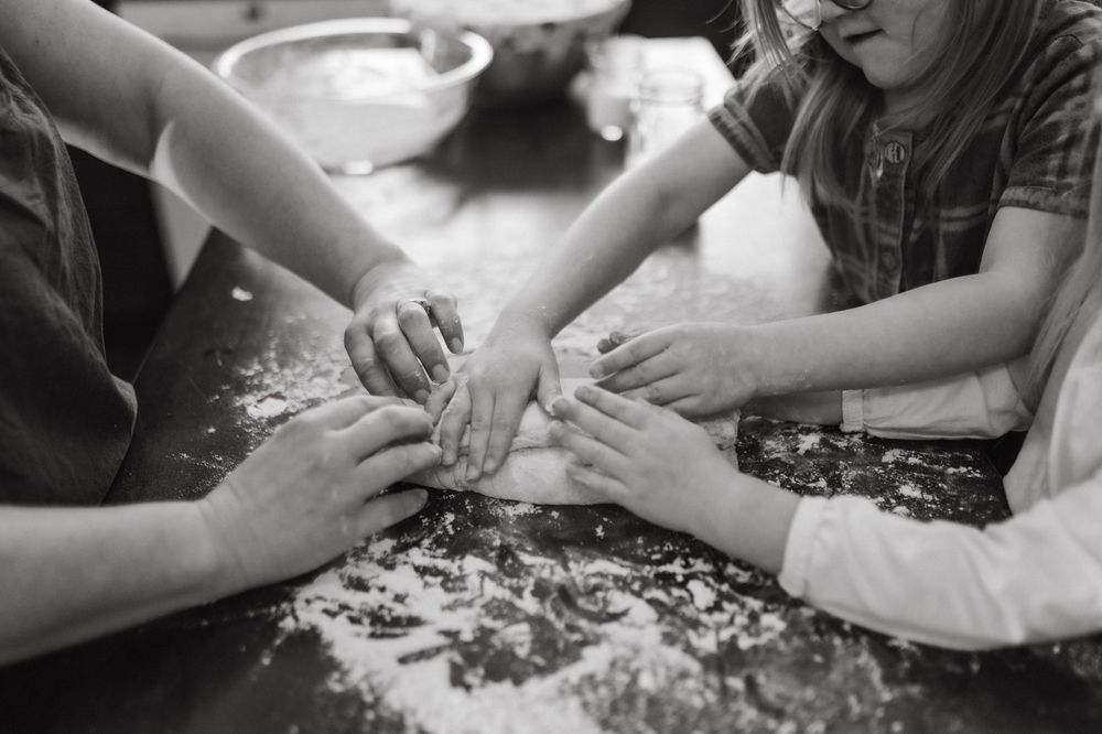 Black and white photo of family hands kneading dough together on a flour-dusted kitchen counter in Johnson City, TN.