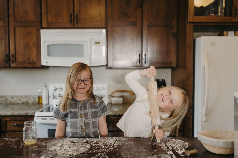 Two young girls baking in a kitchen, one holding a rolling pin with flour on the counter in Johnson City, TN.