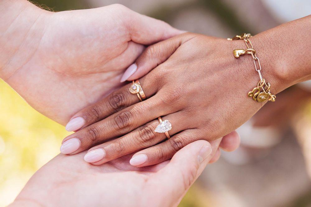 Close-up of engagement ring on woman's hand with gold bracelet and pink manicure.